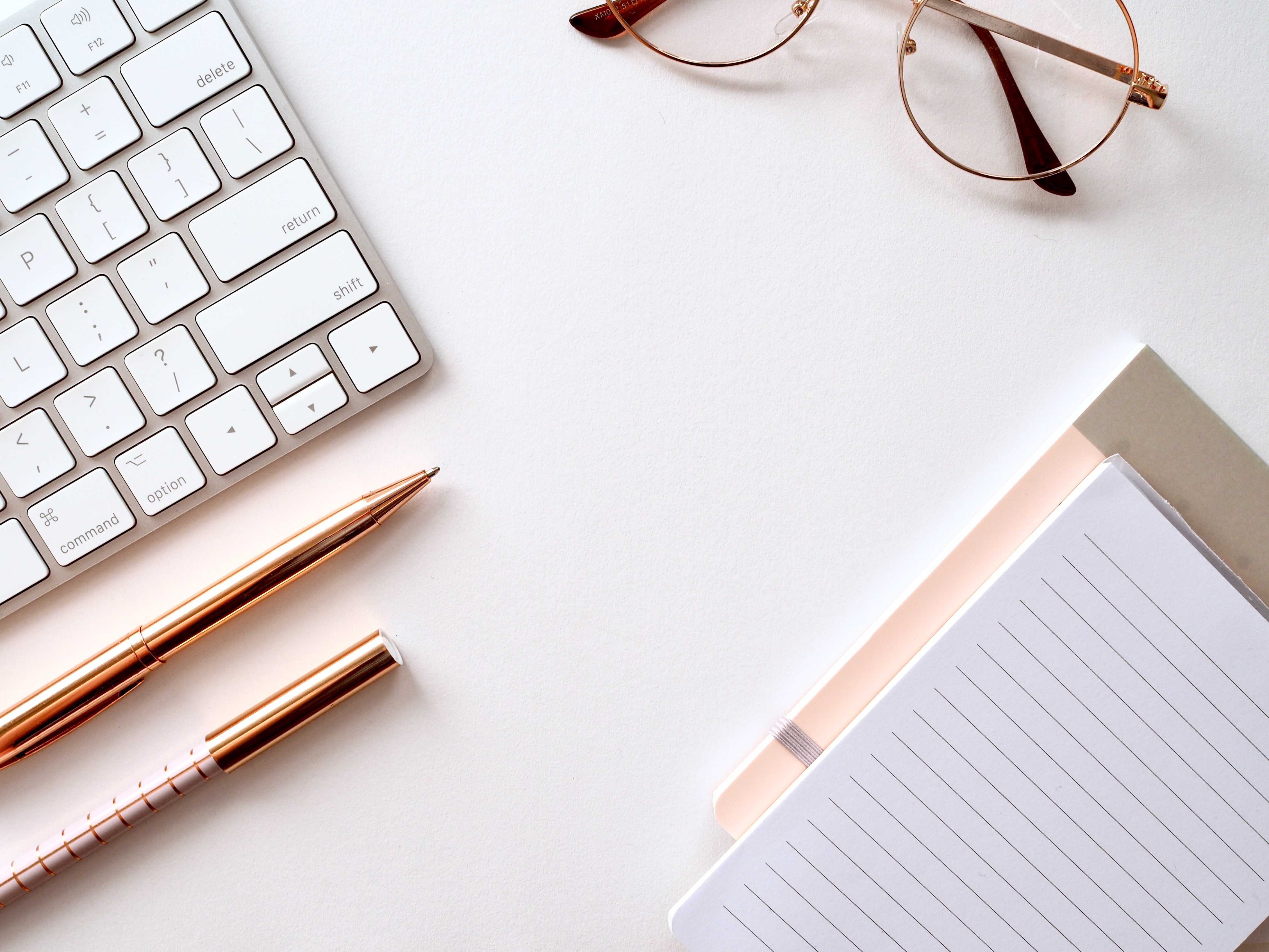 work desk with a keyboard, pen, glasses and notebook